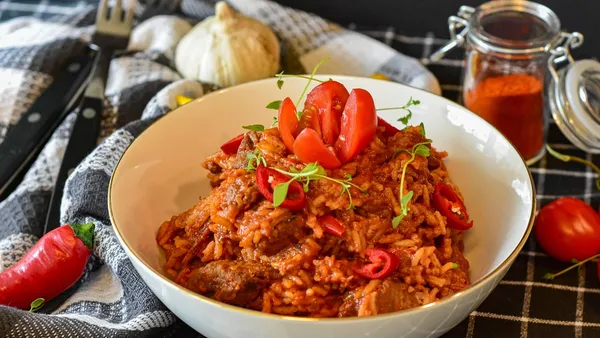 Strogonoff de carne com molho liso e cremoso de tom alaranjado, tiras de filé e champignon, servido com arroz e batata palha